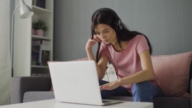 Kulaklıklı genç bir kadın ekran laptopuna bakıyor ve klavyede daktilo yazıyor.