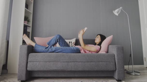 Schöne junge Frau hält Smartphone in der Hand und macht Selfie auf dem Sofa — Stockvideo