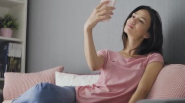 Evdeki kanepede otururken selfie çeken güzel bir kadın.