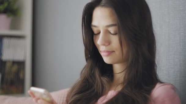 Mujer sentada en un sofá usando su teléfono móvil para enviar mensajes de texto a un amigo . — Vídeo de stock