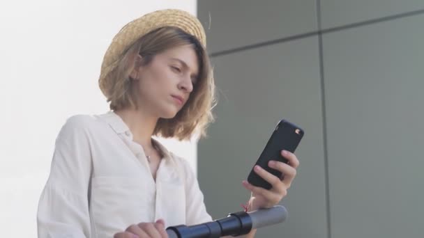 Dolly movimiento de la Mujer está utilizando el teléfono inteligente después de montar en scooter de patada eléctrica — Vídeos de Stock