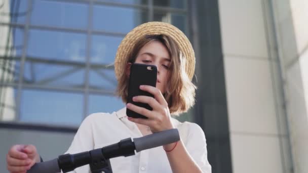 Mujer está utilizando el teléfono inteligente después de montar en scooter de patada eléctrica — Vídeos de Stock