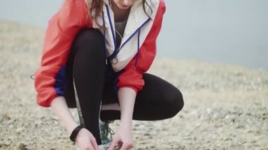 Kadın nehir kenarındaki sahil boyunca koşmaya hazırlanıyor. Koşu ayakkabısı bağlayan sporcu kadın.