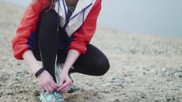 Die Frau bereitet sich darauf vor, am Strand entlang des Flusses zu laufen. Sportliche Frau bindet Laufschuhe — Stockvideo