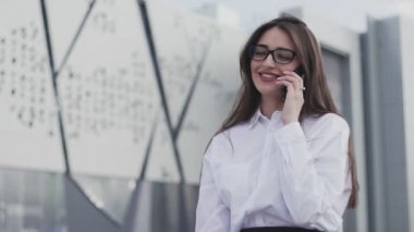 Akıllı telefondan konuşan şık bir kadın. Ofisinin yanındaki bankta oturuyor.