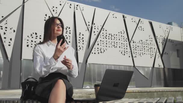 Mulher está chamando por telefone e olhando para a exibição de laptop pensativo ao ar livre — Vídeo de Stock