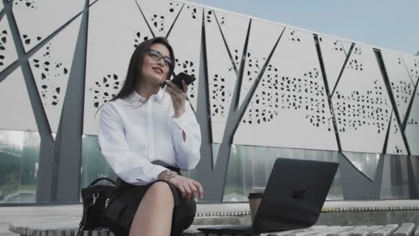 Mulher está gravando mensagem de voz enquanto está sentado no parque com seu caderno — Vídeo de Stock