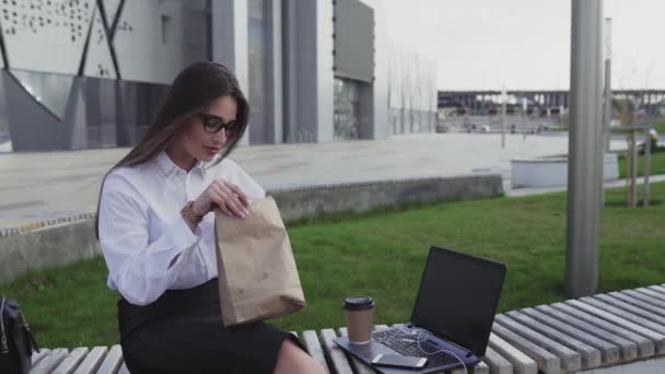 Успешная деловая женщина ест круассан и пьет кофе на открытом воздухе в обеденное время — стоковое видео