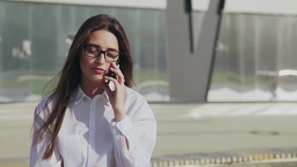 Een succesvolle bedrijfsvrouw die een croissant eet terwijl ze op de mobiele telefoon praat en buiten lacht — Stockvideo