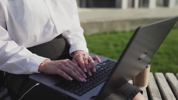 Junge Geschäftsfrau sitzt draußen auf Bank mit Laptop und arbeitet. — Stockvideo