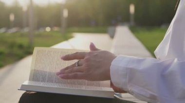 Genç bir kadın parkta bankta oturuyor ve kitap okuyor..