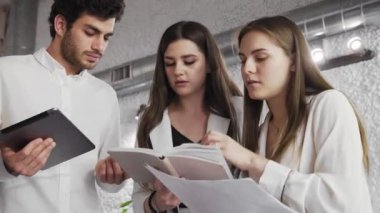 Bir grup genç iş adamı modern bir ofiste bir araya gelip notlara bakıyorlar. iş planlarını tartışan bir grup iş arkadaşı