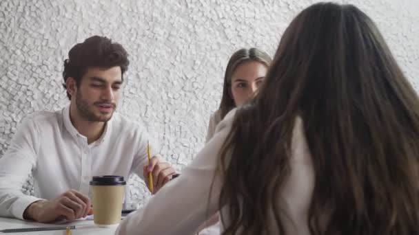 Ofiste toplanan üç genç işadamı küçük bir şirketin ofisinde iş konuşuyorlar. — Stok video