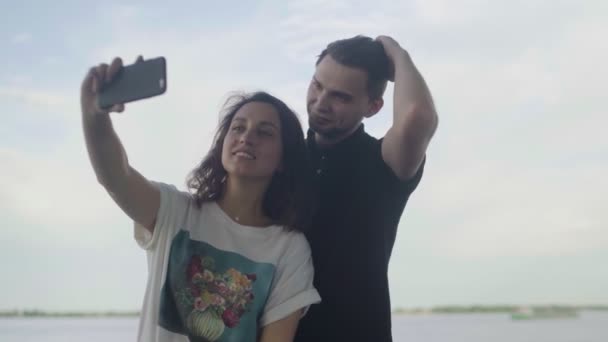 Divertida joven pareja enamorada haciendo fotos cerca del río — Vídeos de Stock