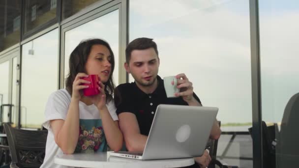 Dois jovens que trabalham com um laptop em um café e bebem café — Vídeo de Stock