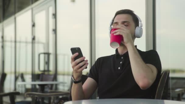 Beau jeune homme avec casque utiliser téléphone assis dans le café — Video