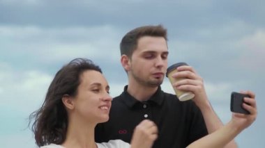 Telefonda fotoğraf çeken ve sokakta kahve içen bir çift.