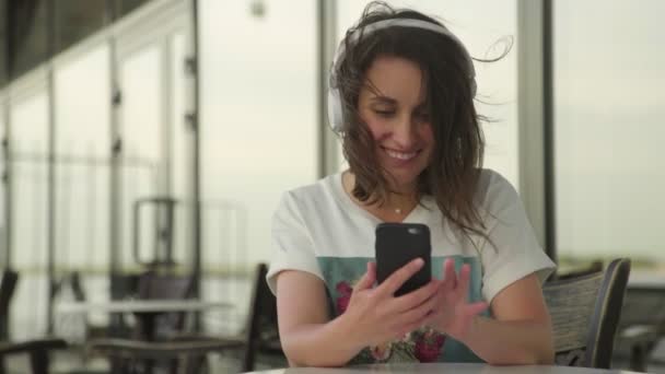 Mujer joven en auriculares escuchando música y charlando en el teléfono inteligente — Vídeo de stock