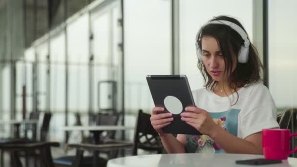 Kulaklıklı düşünceli kadın kafede tablet kullanıyor. — Stok video