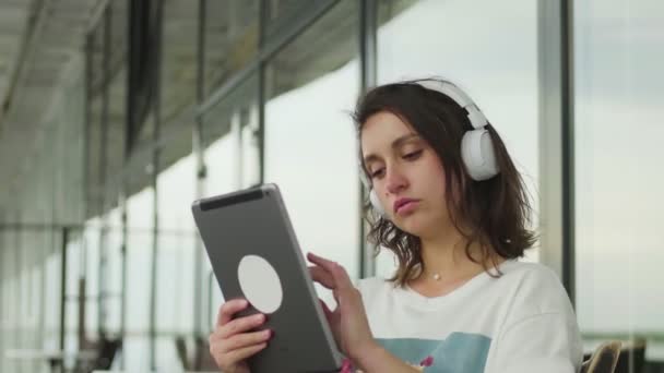 Açık kafede tablet pc dokunmatik ekranı kullanan kulaklıklı gülen Avrupalı kadın — Stok video