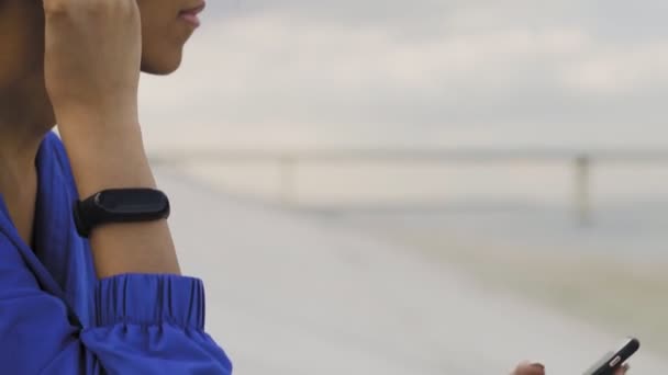 Mujer corredora afroamericana con auriculares y reloj inteligente descansando después de correr en el parque — Vídeo de stock