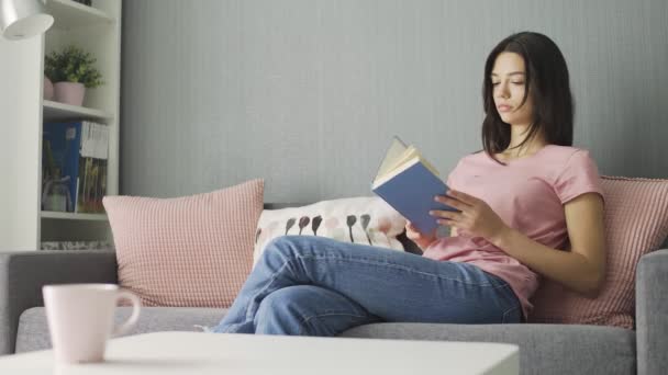 Женщина читает книгу и пересаживается на диван дома — стоковое видео