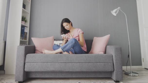Mujer linda joven usando el teléfono mientras está sentado en un sofá en casa . — Vídeo de stock