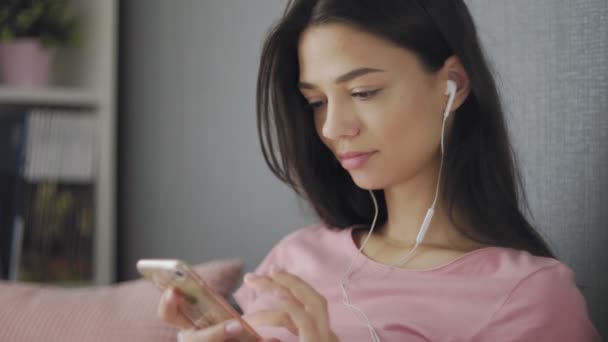 年轻时尚女性，戴着耳机，在家听音乐和浏览手机 — 图库视频影像