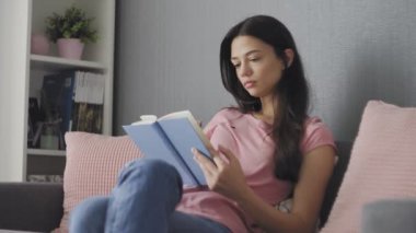 Güzel genç bir kadın kanepede otururken hüzünlü bir kitap okuyor.