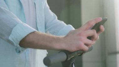 Elektrikli scooterlı bir adam telefonunu açık havada kullanıyor.