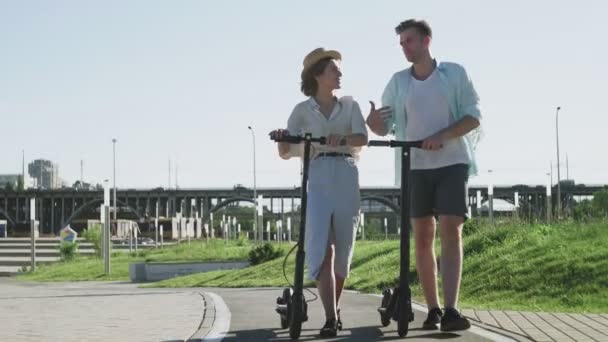 여름 공원에서 전기 스쿠터를 타고 행복 한 부부가 걷는 모습 — 비디오