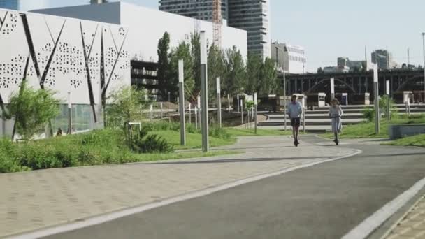 Happy Couple rijden op hun elektrische scooters in het zomerpark — Stockvideo