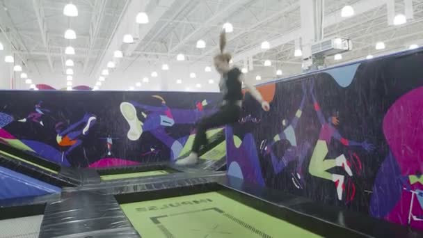 Vrouw duwt van de muur en springt op de trampoline — Stockvideo