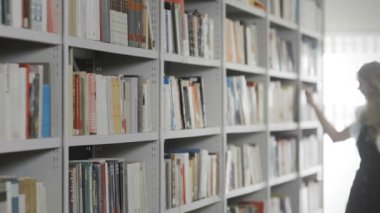 Güzel sarışın kız kütüphanedeki raftan kitap alıyor.