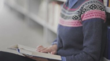 Genç Afrikalı Amerikalı kadının Dolly hareketi üniversite kütüphanesinde yerde oturmuş kitap okuyor..