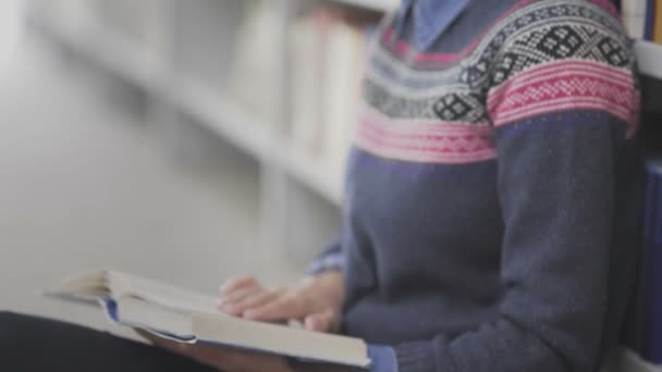 Dolly move de la jeune femme afro-américaine lit un livre assis sur le sol dans une bibliothèque universitaire . — Video