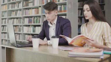 Okuldaki bir kütüphanedeki öğrenciler bilgisayar ve kitap kullanıyor ve projeler için konuşuyorlar