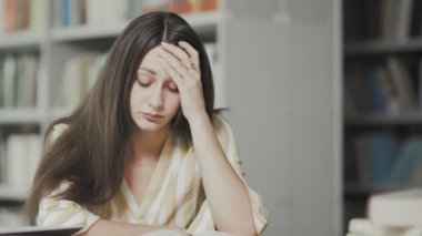 Yorgun genç bayan üniversite kütüphanesinde sınava hazırlanıyor.