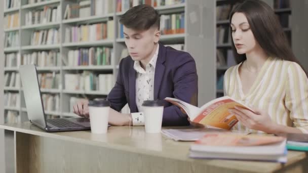 Estudiantes en una biblioteca en la escuela usan computadoras y libros y hablan para proyectos — Vídeo de stock