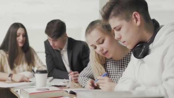 Två män och två kvinnor högskolestudenter studerar med böcker och skriva anteckningar om bärbara datorer i gymnasiebiblioteket mot bokhylla. — Stockvideo