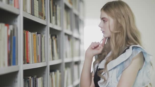 Junge attraktive blonde Studentin nimmt zwei Bücher aus dem Regal in der Bibliothek — Stockvideo