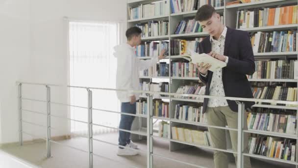 Dos jóvenes estudiantes leyendo un libro en la biblioteca — Vídeos de Stock