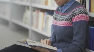 Afrikalı Amerikalı kadının Dolly hareketi okul kütüphanesinde yerde oturmuş kitap okuması..