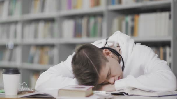 Trött kille somnar medan han studerar på biblioteket på högskolan — Stockvideo