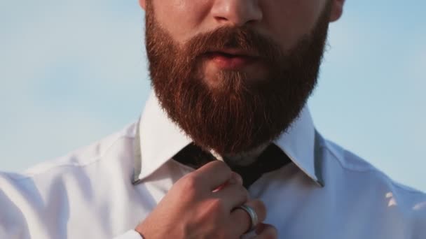 सफेद शर्ट में दाढ़ी वाला आदमी आउटडोर गर्दन बांध रहा है — स्टॉक वीडियो