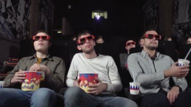 Üç arkadaş film izliyor ve patlamış mısır yiyorlar.