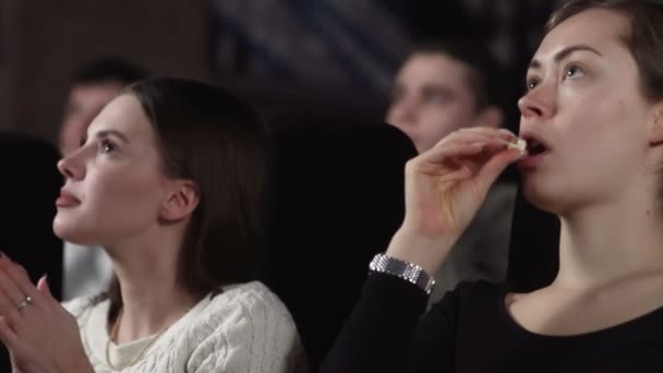 Primer plano de tres amigas guapas están comiendo palomitas de maíz y viendo una película en el cine — Vídeos de Stock