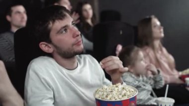 Dolly hareket halindeki insanlar patlamış mısır yiyip sinemada film izliyorlar.