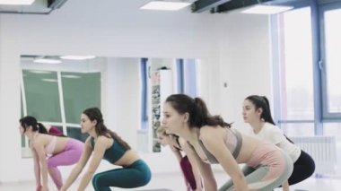 Yoga öğrencileri Virabhadrasana 'nın ışık stüdyosunda Savaşçı pozu üzerinde çalışıyorlar..