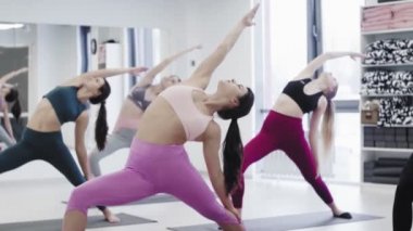 Yoga öğrencileri Virabhadrasana 'nın ışık stüdyosunda Savaşçı pozu üzerinde çalışıyorlar..